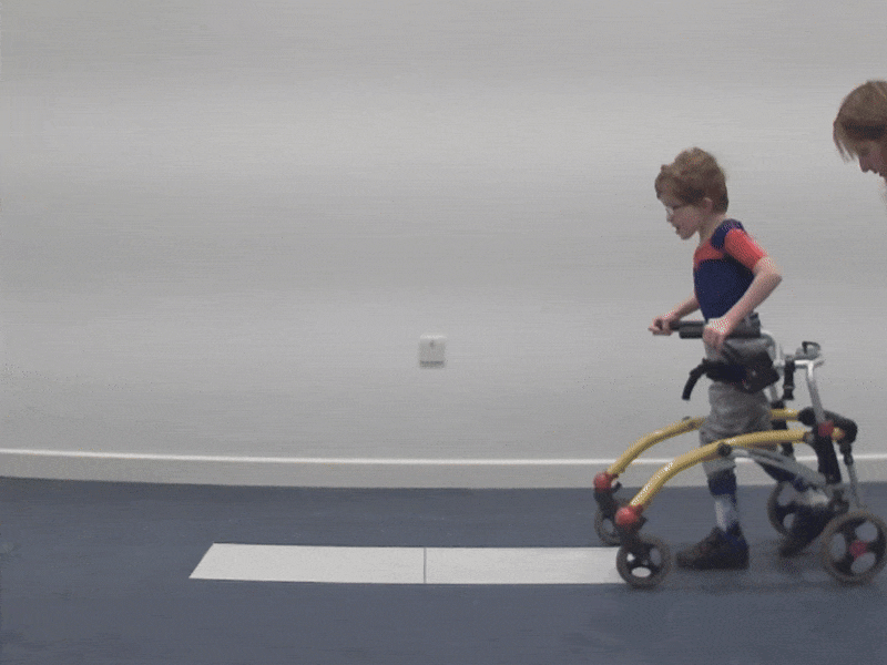 A young boy with cerebral palsy walks in a gait lab with the help of his walking frame and his new orthotics